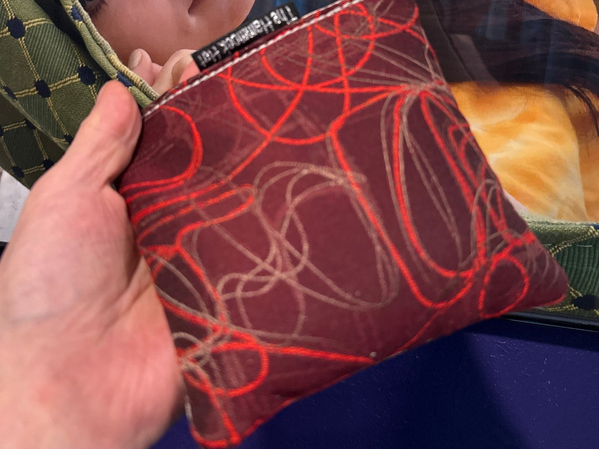 Premium Scribble Firecracker Red cornhole bag held in hand, landscape product photo