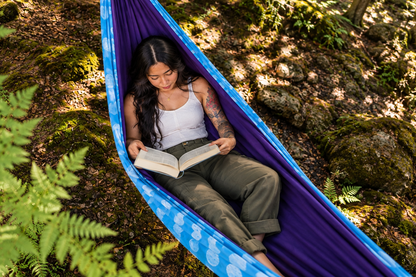 Mini Bo reading in the Azure Solstice Premium Hammock in a fern-filled woodland