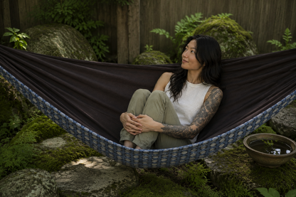 Botanica Solstice Premium Hammock with the model curled comfortably in a quiet garden