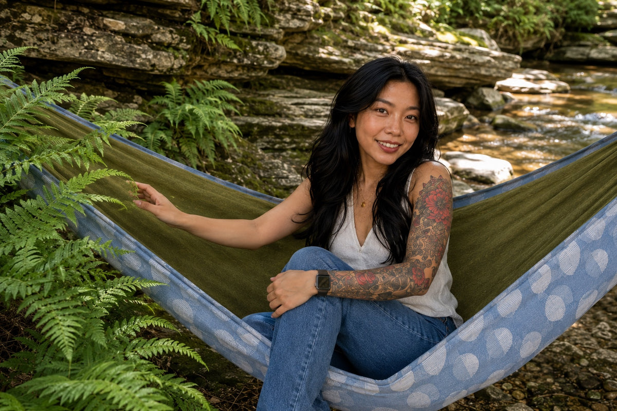 Woman seated in Fernwater Solstice Premium Hammock beside lush ferns