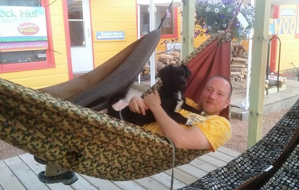 A customer relaxing with a dog in a Hammock Hut hammock outside the shop.