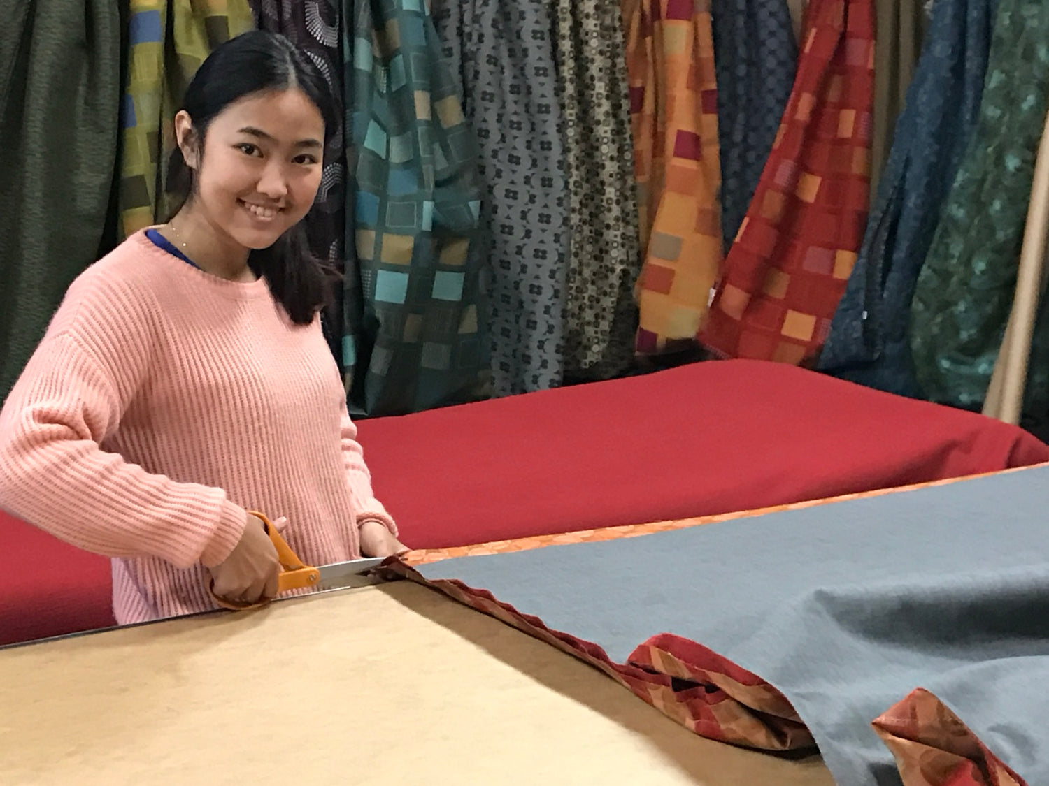 Woman cutting fabric by hand in the Hammock Hut workshop with finished hammock fabrics hanging in the background.