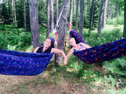 Two friends smiling from colorful Hammock Hut hammocks in the woods.