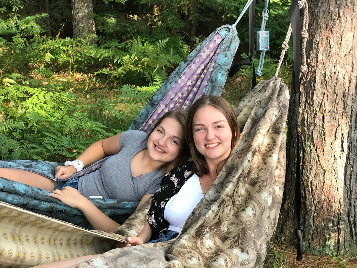 Two friends relaxing side by side in handmade Hammock Hut hammocks among the pine trees.