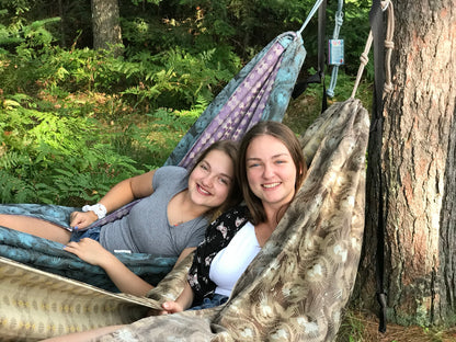 Two friends relaxing side by side in handmade Hammock Hut hammocks among the pine trees.