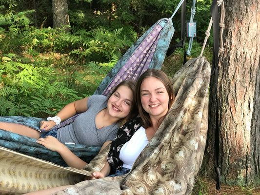 Two friends relaxing side by side in handmade Hammock Hut hammocks among the pine trees.