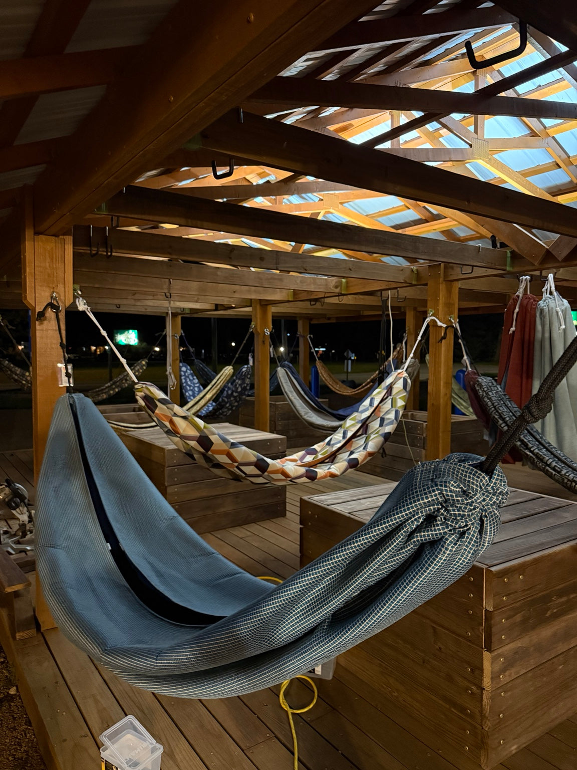 Hammock Hut outdoor display filled with handmade hammocks under a timber roof at night.