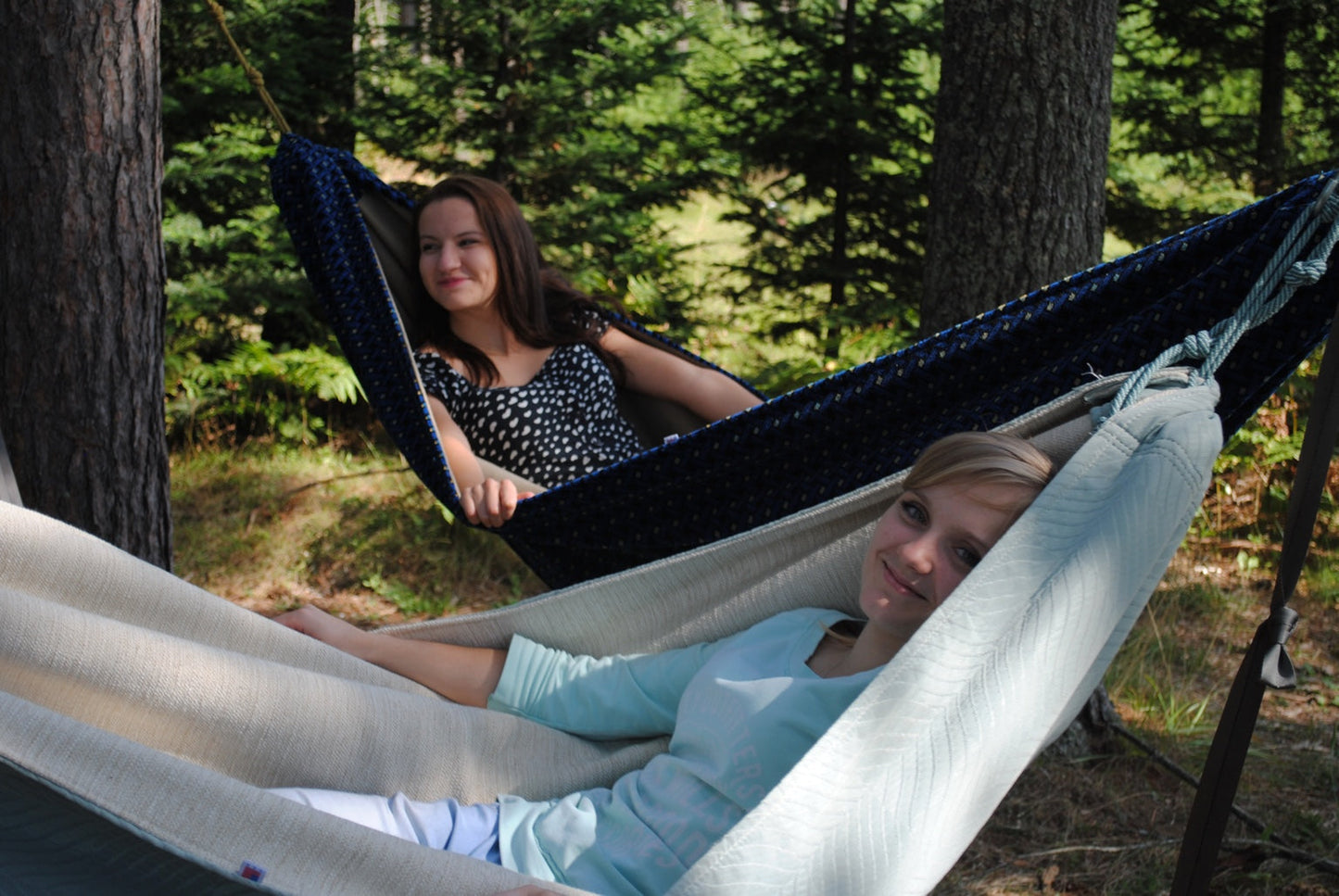 Two friends relaxing in Hammock Hut hammocks among Northwoods trees.