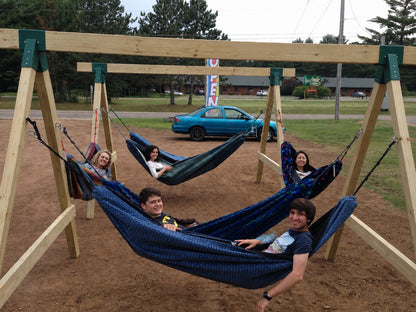 Five people relaxing in hammocks on freestanding wooden stands built with green hammock stand brackets.