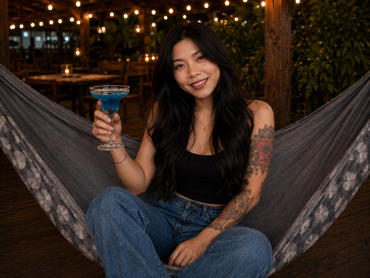 Moonstone Solstice Premium Hammock with smiling model holding a blue drink under warm string lights